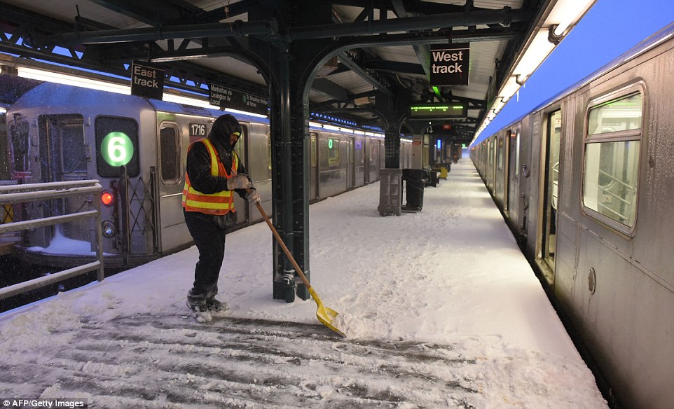 A NYC transit worker shovels snow from an above-ground subway platform in New York City before the above-ground trains were closed on Saturday