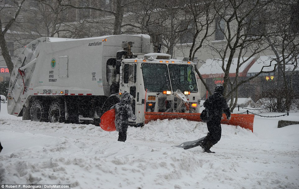 A parent and their child dragging sleds cross the road in Manhattan as a snow plow makes its way past on Saturday