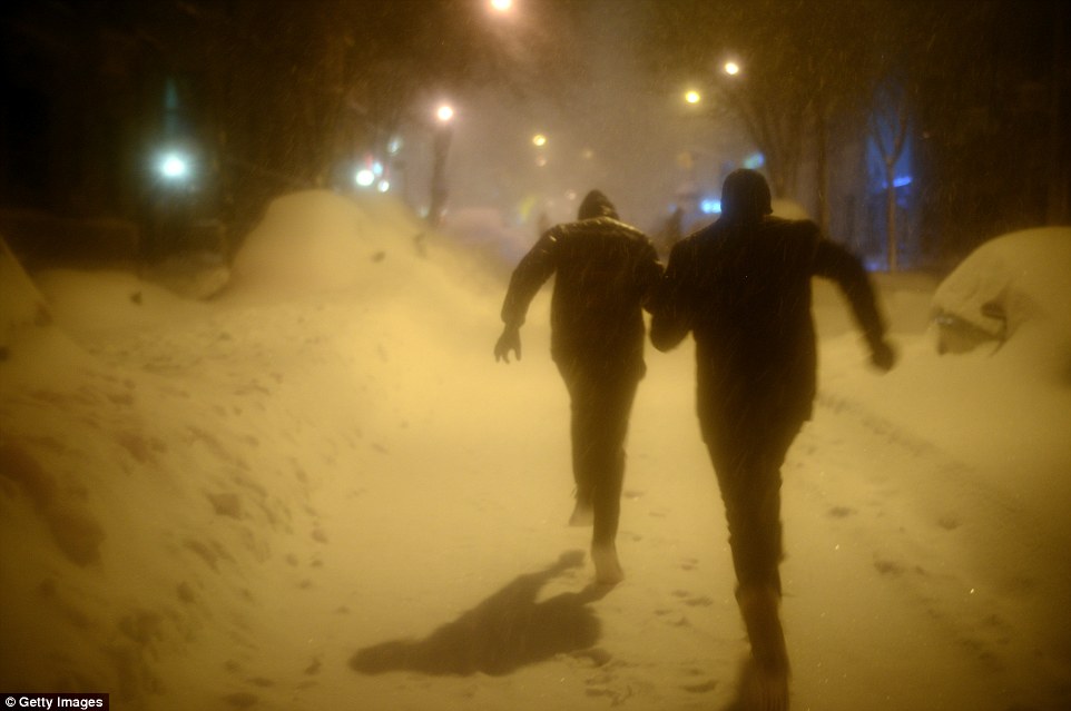 Two young men run along West 83 street which is covered in snow after a day of constant snow fall on Saturday