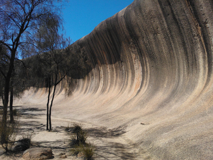 The shape of the rock is not caused by a wave phenomenon, rather its rounded wave-like shape was formed by subsurface chemical weathering