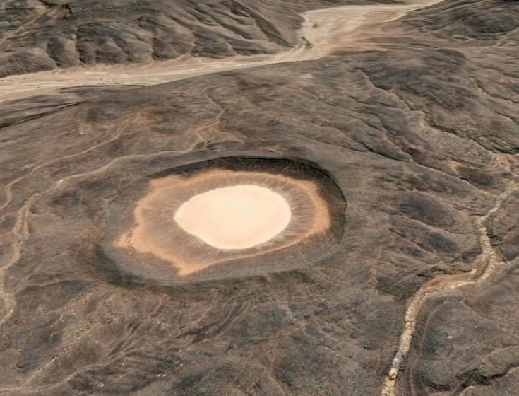 A meteorite crater named Amguid Crater. This is roughly 65 meters deep and around 500 to 530 meters in diameter (measured with Google Earth).